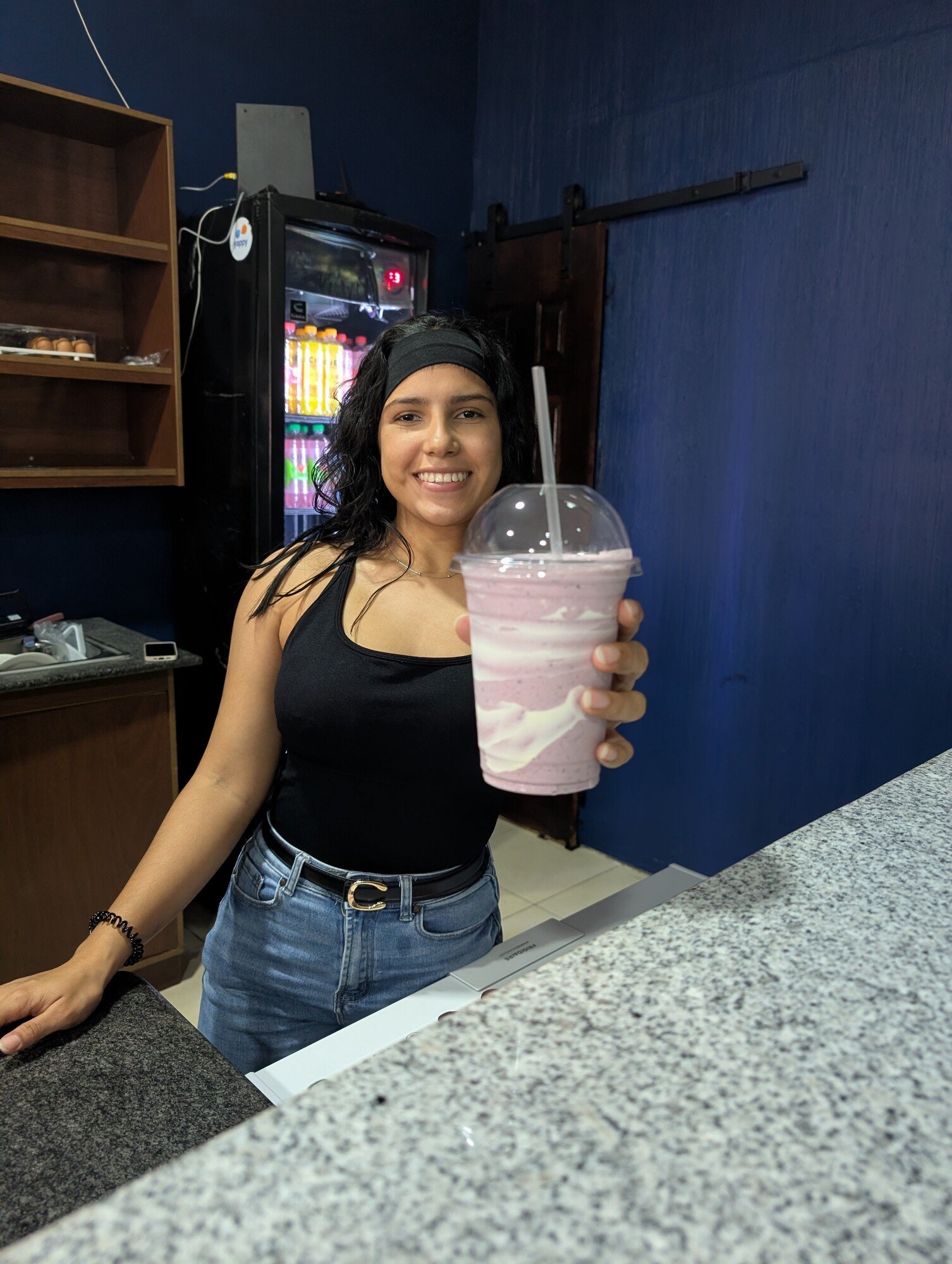 Persona sonriente muestra un batido rosado en la barra de la cafetería