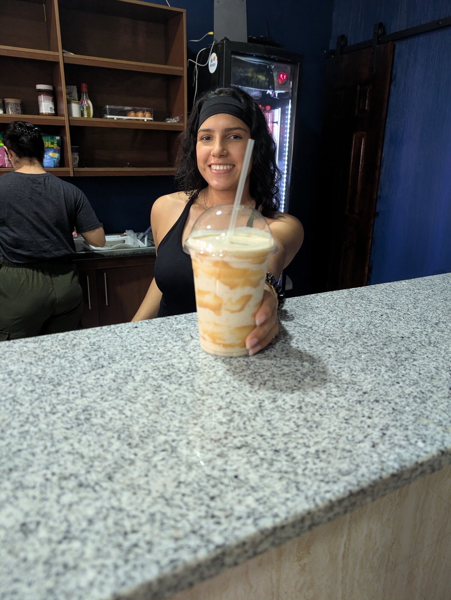 Persona muestra un batido de color naranja sobre la barra de la cafetería