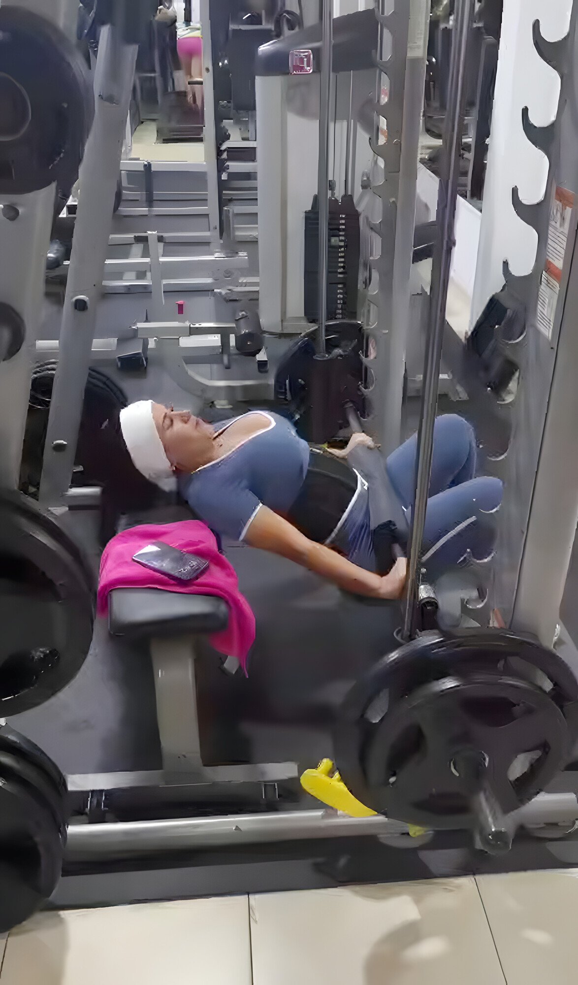Una mujer hace hip thrust en la máquina Smith con discos, con la espalda apoyada en un banco