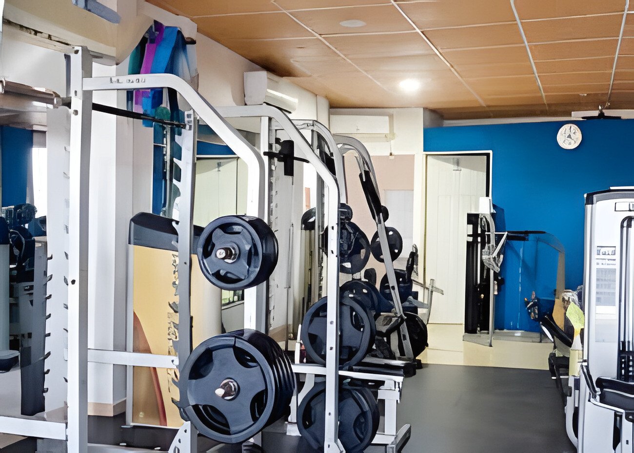 Una zona de fuerza con racks, barras y discos frente a la pared azul de la sala